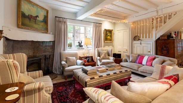 Ein gemütliches Wohnzimmer mit Kamin, gestreifte Armlehnstühle, einer Couch und einer Treppe mit Lichterketten.