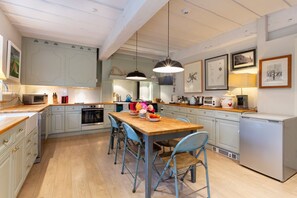 A modern kitchen with white cabinetry, a wooden dining table, blue chairs, and pendant lighting.