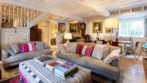 Ein gemütliches Wohnzimmer mit zwei Sofas, einem Couchtisch mit Büchern, einer Treppe und einem Essbereich mit einer Lampe.