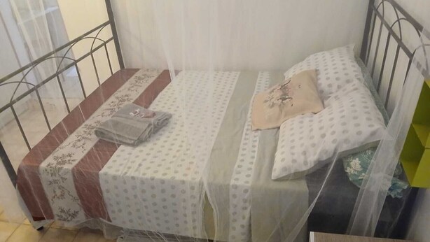 Un llit individual amb una mosquiter, una catifa rayada i una taula de fusta petita.