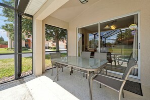 An outdoor patio with a glass table and chairs, a door leading to a covered area, and a view of a residential neighborhood. - 5BR Private Pool Home Near Disney | FREE Pool Heat | Gated Resort (Davenport)