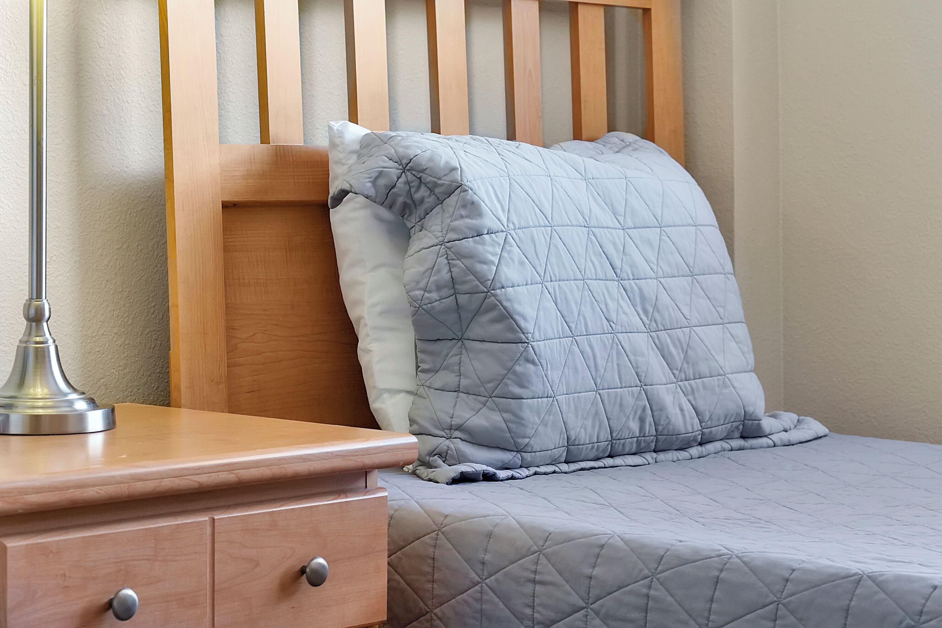 A neatly made bed with a quilted gray blanket and a wooden headboard.