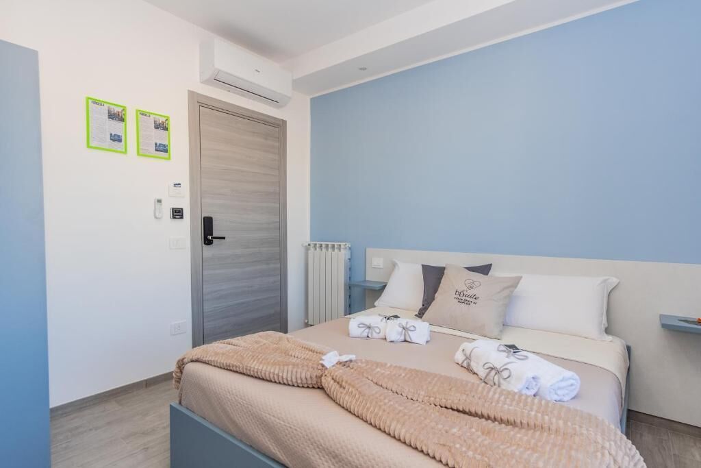 Quarto com uma cama, um radiador, uma porta e dois avisos em molduras na parede.