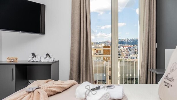 Une chambre d’hôtel équipée d’un lit, d’un téléviseur fixé au mur, d’un bureau avec un ordinateur et offrant une vue sur la ville grâce à de grandes fenêtres.