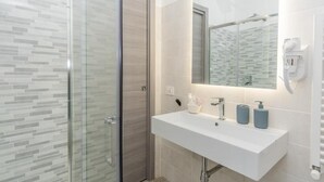 Une salle de bain moderne avec une douche à parois de verre, un lavabo blanc avec un miroir au-dessus et un porte-serviettes.