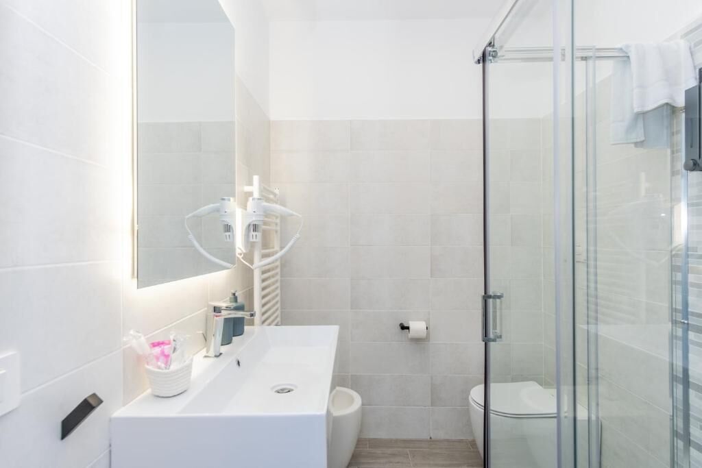 Un baño moderno con cabina de ducha de vidrio, lavamanos blanco y espejo.