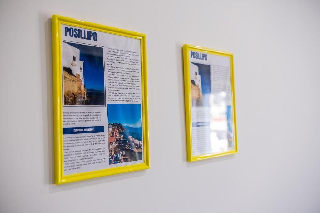 Deux affiches d’information encadrées sont accrochées au mur. Elles sont intitulées « POSILLIPO » et présentent du texte et des images d’une ville côtière.