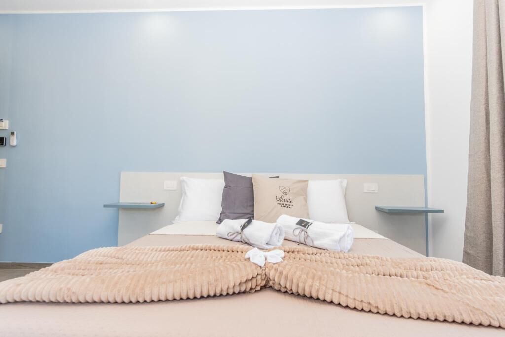 A hotel room with a bed, pillows, a blanket, and a sign on the headboard.