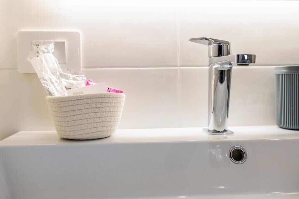 Un bagno con un lavandino bianco, un rubinetto cromato e un portasapone bianco con superficie strutturata.