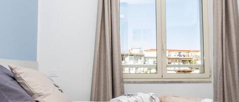 A hotel room with a bed, pillows, and a window with curtains.