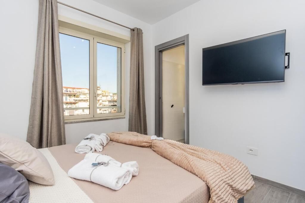 A hotel room with a bed, a TV mounted on the wall, and a window with curtains.