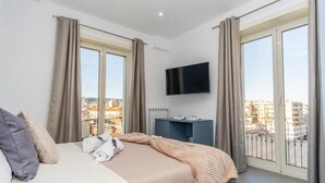 Une chambre à coucher avec un lit, une télévision et une vue sur la ville grâce à de grandes fenêtres.
