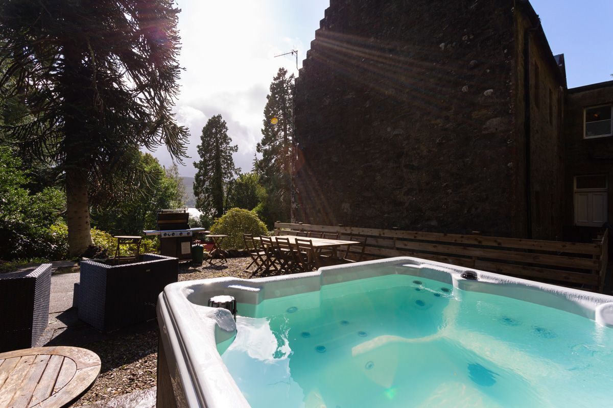Un bain à remous entouré de meubles de jardin et d’un mur en pierre.