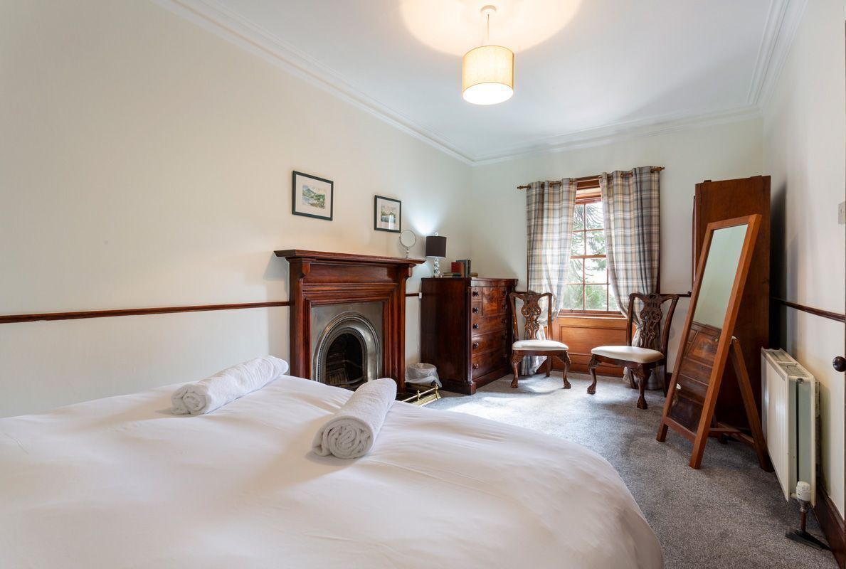A hotel room with a bed, a fireplace, a mirror, a dresser, and a window with curtains.