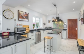 A modern kitchen with a central island, stainless steel appliances, and a large wall clock.