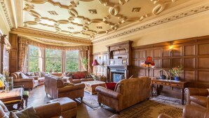 A spacious living room with leather sofas, a fireplace, and a large window overlooking greenery. - Argyll Country House (Clachan)
