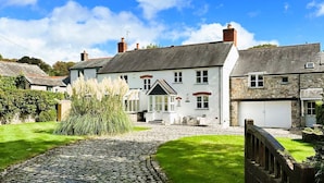 A traditional stone house with a cobblestone driveway, a small garden, and a stone wall.