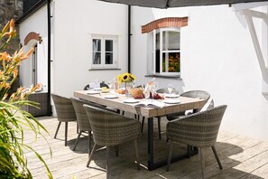 An outdoor dining area with a wooden table set for four, surrounded by wicker chairs. - Sea Mist House - Six Bedroom Villa, Sleeps 14 (Charlestown)