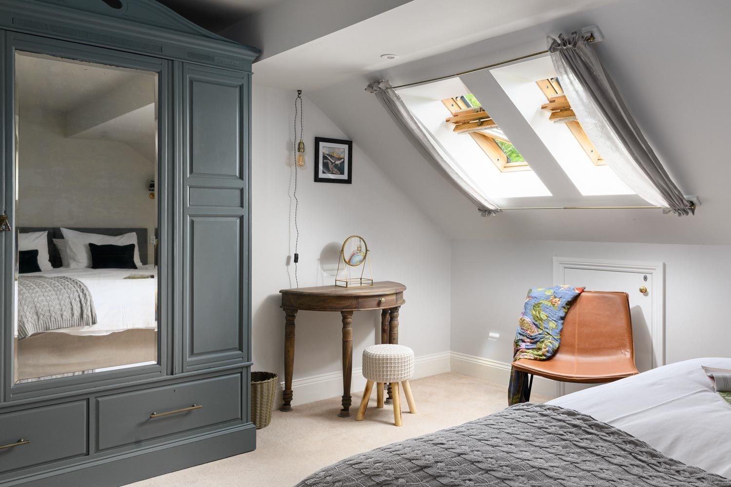 Een slaapkamer met een grote inbouwkast, een klein tafeltje met spiegel, een kruk, een stoel en een bed.
