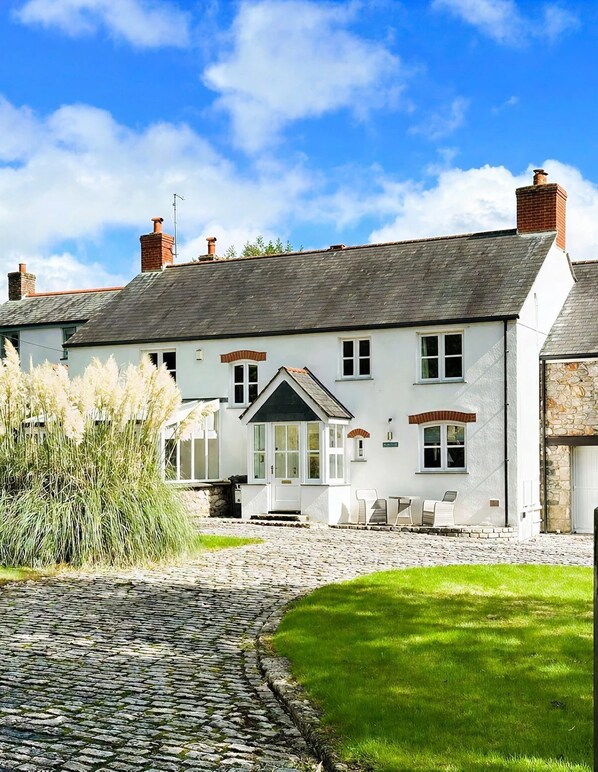 A traditional white building with a stone facade, a stone driveway, and a well-maintained lawn.