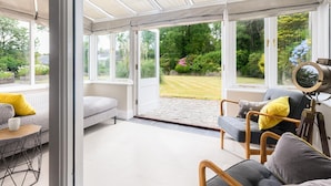 A conservatory with a seating area, a camera on a tripod, and a view of a garden.