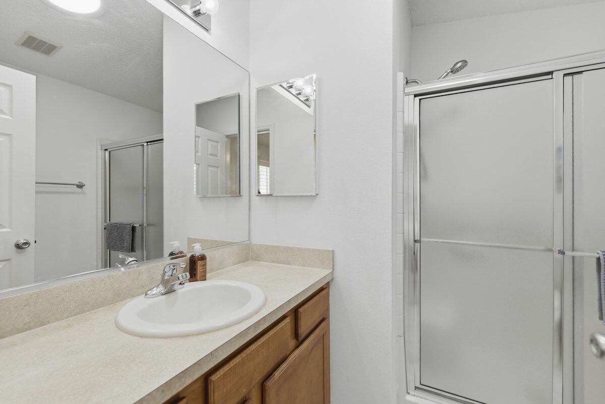 A bathroom with a white sink, two mirrors, a shower enclosure, and wooden cabinets.