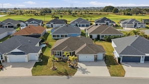 Zona residencial con casas de techo a dos aguas, patios delanteros y un campo de golf al fondo.
