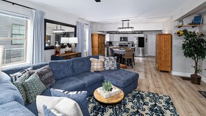 A modern living room with a blue sectional sofa, a dining area with a wooden table, and a kitchen with white cabinets and stainless steel appliances. - Private Updated Home W/ Dedicated Work Space - Close to Downtown (Chattanooga)