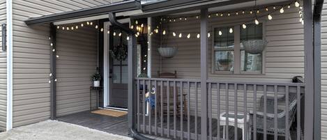 A house with a covered porch, string lights, wicker furniture, and a basket hanging from the ceiling.