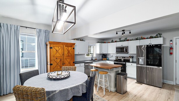 A modern kitchen with white cabinets, stainless steel appliances, a wooden island, and a dining area with wicker chairs and a table. - Private Updated Home W/ Dedicated Work Space - Close to Downtown (Chattanooga)