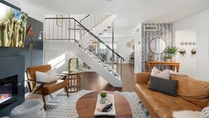 Uma sala de estar moderna com lareira, um sofá de couro marrom, uma mesa de centro e uma escada que leva a um andar superior.