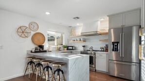 Uma cozinha moderna com uma ilha central, banquetas de bar, eletrodomésticos de aço inoxidável e detalhes decorativos nas paredes.