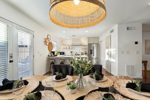 Una cocina moderna con armarios blancos, un refrigerador de acero inoxidable y un comedor con una mesa redonda para cuatro.
