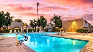 Piscina com espreguiçadeiras e céu ao pôr do sol.