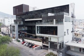 A modern multi-story building with large glass windows, a parking area with several cars, and a visible commercial space on the ground floor. - ¡Luxury with Terrace! King Bed & Sofa Bed 4ppl (Monterrey)