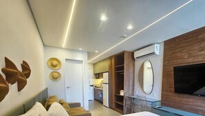 A modern hotel room with a bed, a TV, a wardrobe, a desk, and a kitchenette.