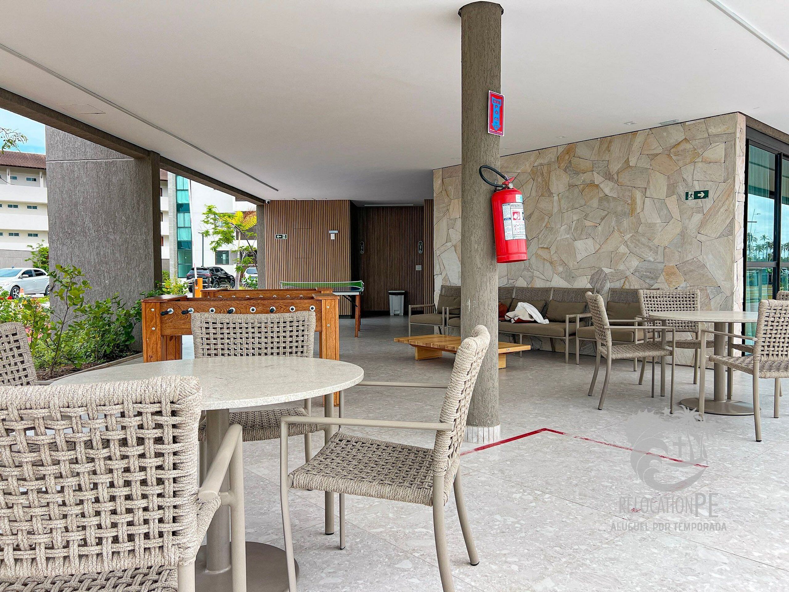 A modern indoor area with wicker furniture, a fire extinguisher, and a stone wall.