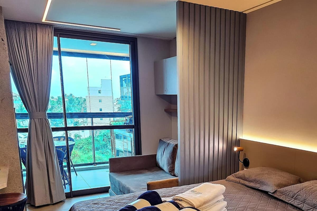 Habitació d'hotel moderna amb una finestra gran, un llit, zona de seients i una televisió.