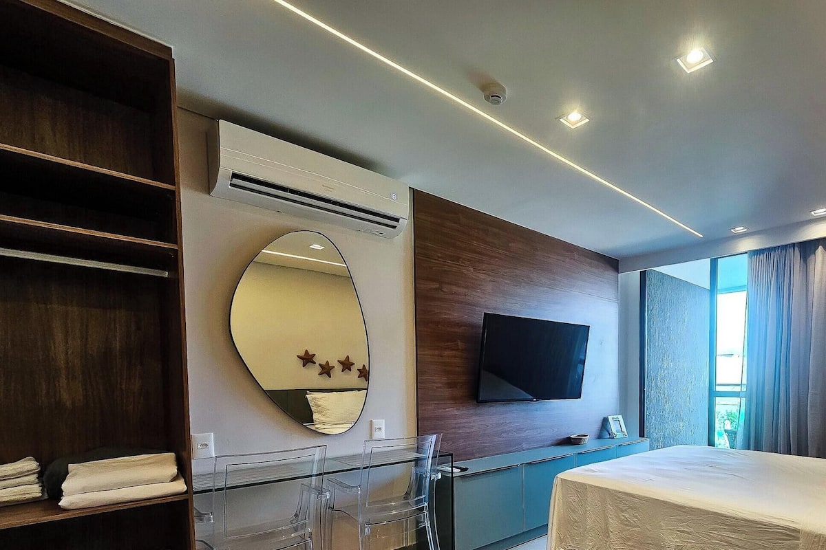 Habitació d'hotel moderna amb un llit, una televisió, un mirall gran i una finestra amb cortines.