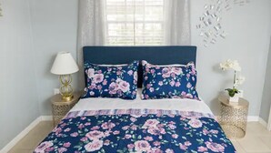 Een slaapkamer met een bed, bloemenbeddengoed, een nachtkastje, een lamp en een decoratief wandobject.