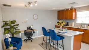 Een moderne keuken met een centraal eiland, blauwe barkrukken en een potplant.