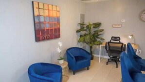 Een woonkamer met blauwe fauteuils, een grote potplant, een schilderij en een wandklok.