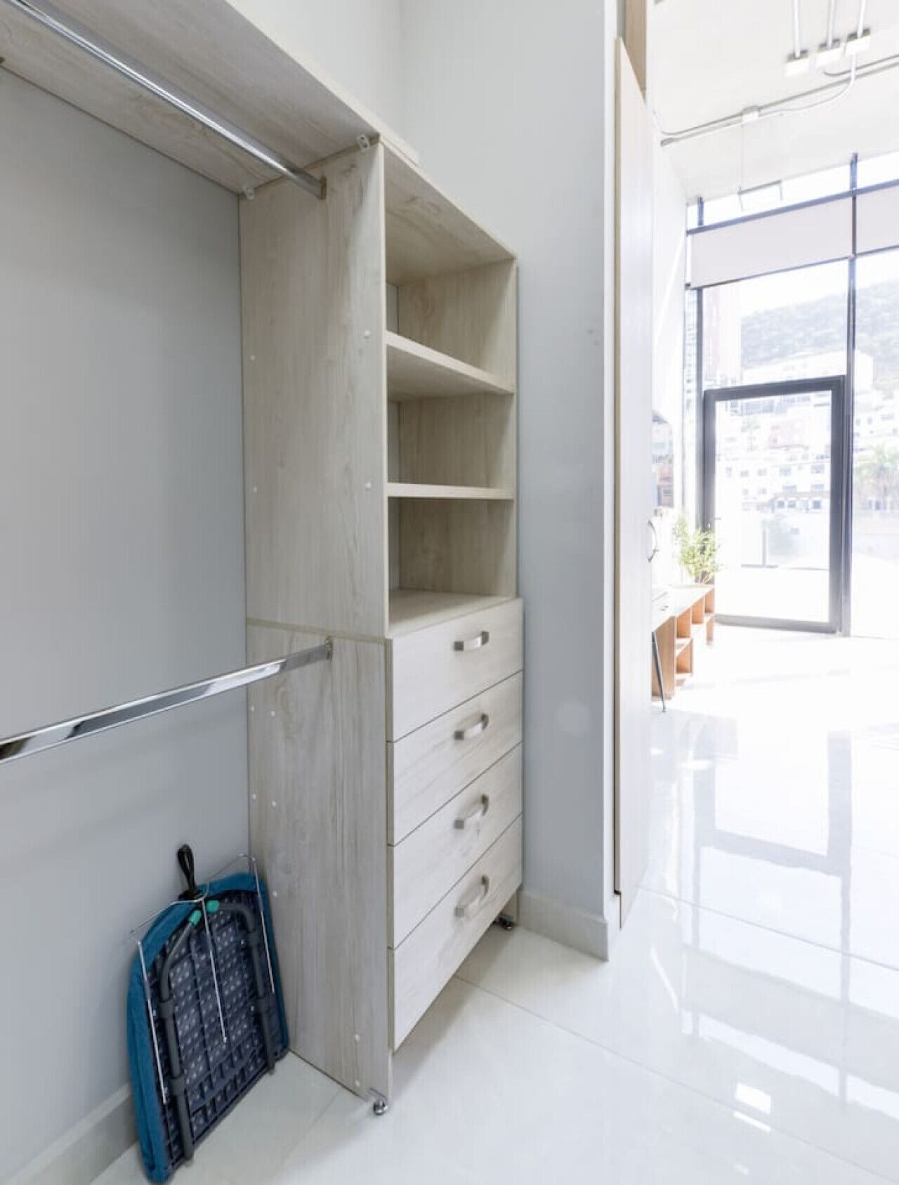 Een moderne, minimalistisch ingerichte kamer met een inbouwkast, een klein tafeltje met een stoel en een stadszicht door een groot raam.