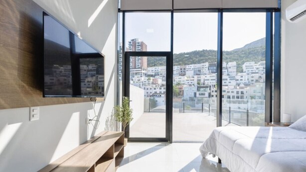 Ein modernes Schlafzimmer mit großem Fenster, einem Flachbildfernseher, einem Nachttisch und einem Bett.