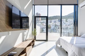 Ein modernes Schlafzimmer mit großem Fenster, einem Flachbildfernseher, einem Nachttisch und einem Bett.