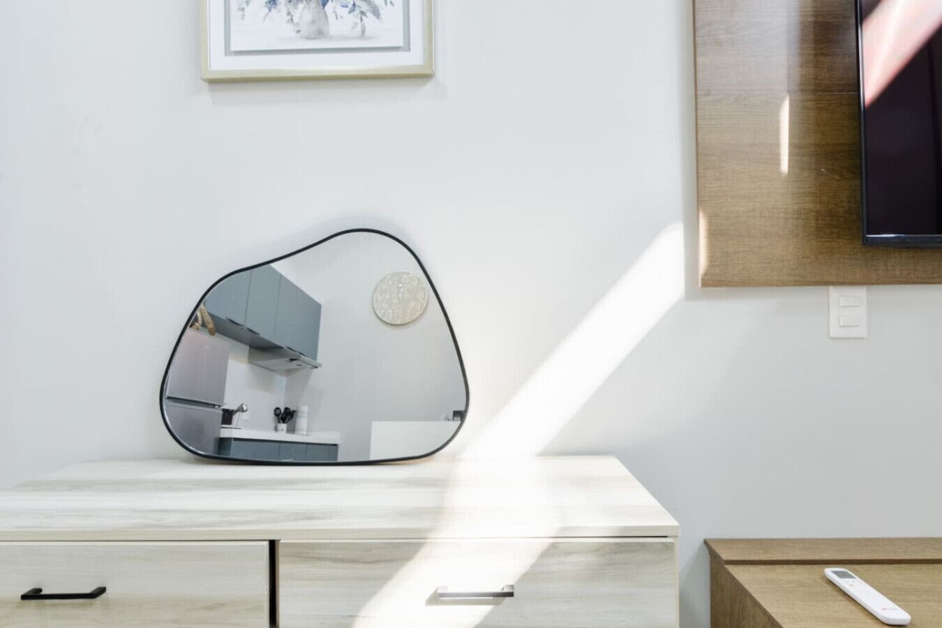 Un baño moderno con un espejo original, un tocador de madera y un cuadro enmarcado en la pared.