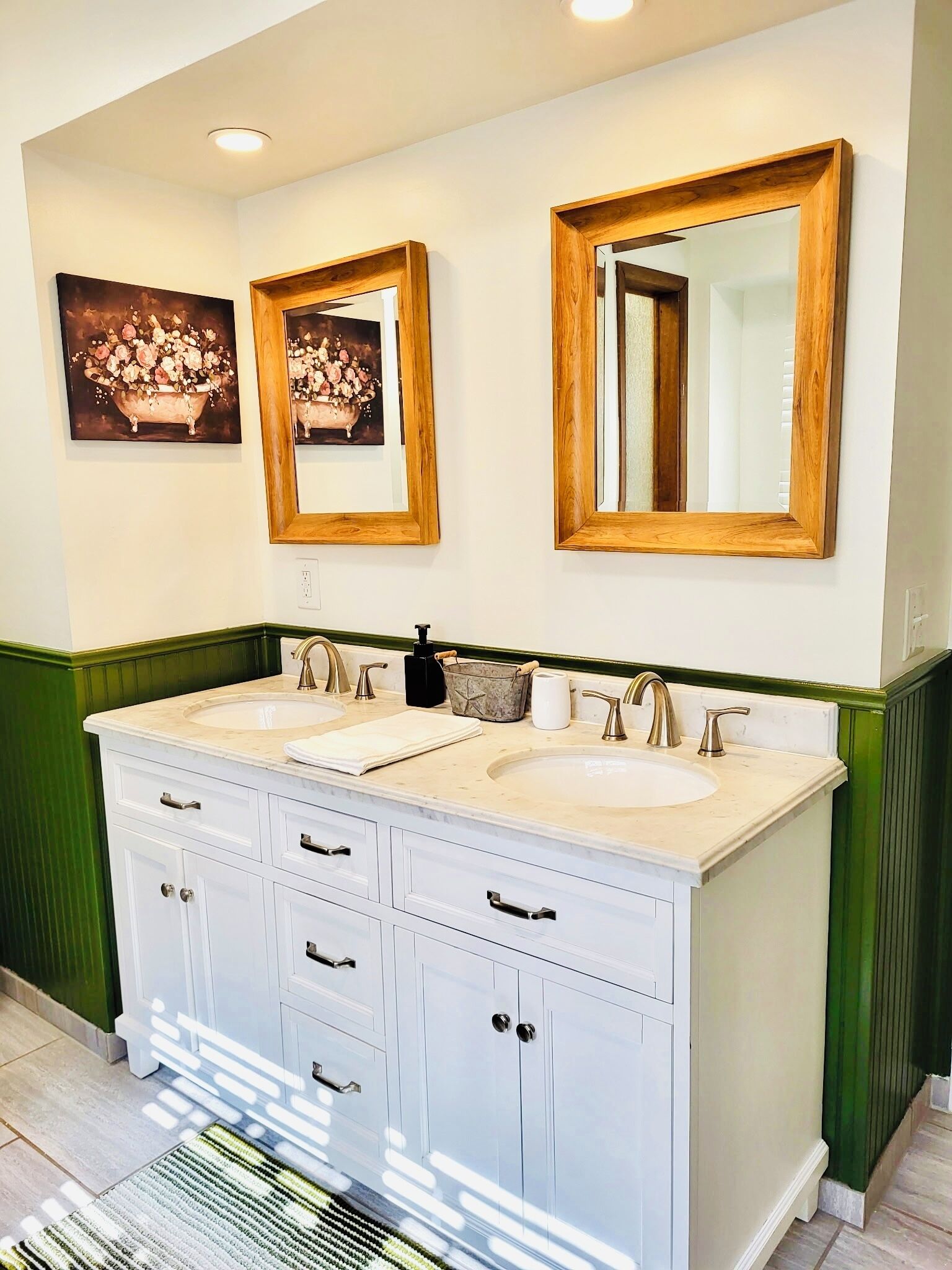 A bathroom with two sinks, a large mirror, and a painting of flowers on the wall.
