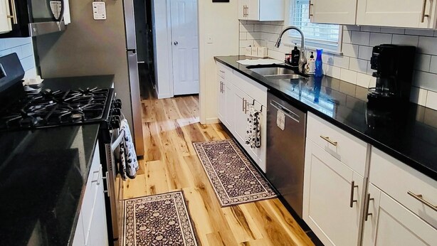 A modern kitchen with white cabinets, a black countertop, stainless steel appliances, and wooden flooring.