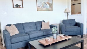 A modern living room with a grey sofa, a matching armchair, a wooden coffee table, and a painting on the wall.