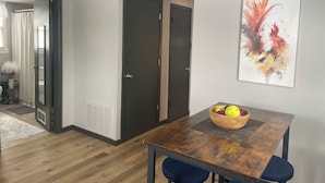 Una habitación de hotel moderna con una mesa de comedor de madera, un frutero y un cuadro abstracto llamativo en la pared.